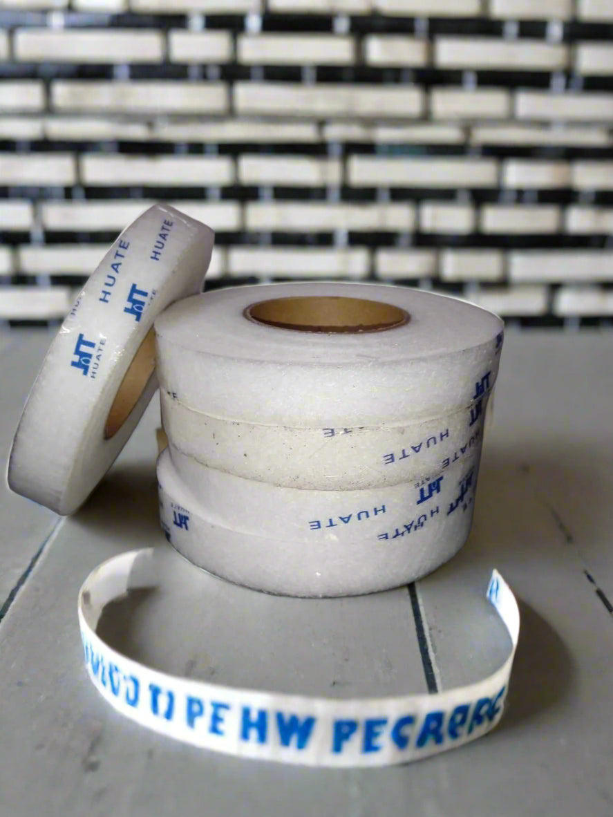 Two rolls of white tape with blue text on a metallic surface against a tiled wall.